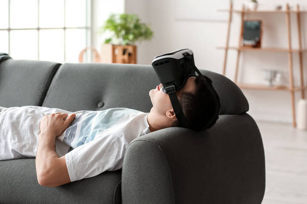 Joven con gafas de realidad virtual tumbado en el sofá en casa - Foto, imagen