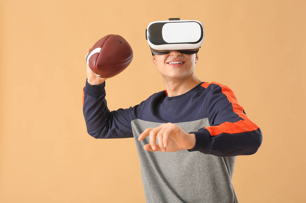 Sportieve jongeman met virtual reality bril spelen Amerikaanse voetbal op kleur achtergrond - Foto, afbeelding