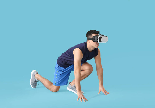 Sporty young man with virtual reality glasses on color background - Foto, Imagem