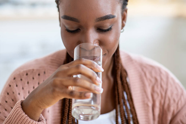 Освежающий напиток. Молодая чернокожая леди пила воду из стакана дома - Фото, изображение