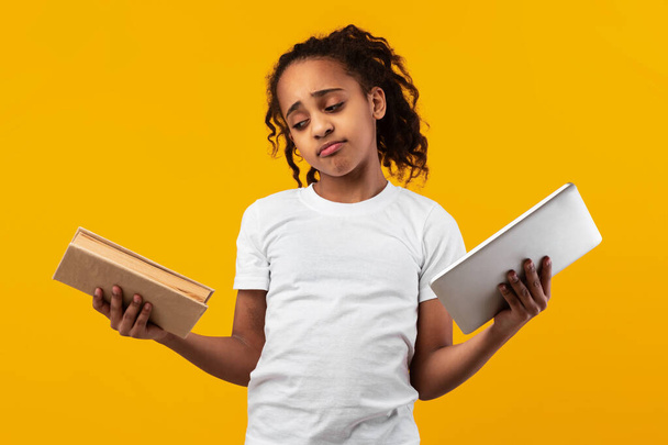Unsicheres schwarzes Mädchen steht mit Buch und Tablet im Studio - Foto, Bild