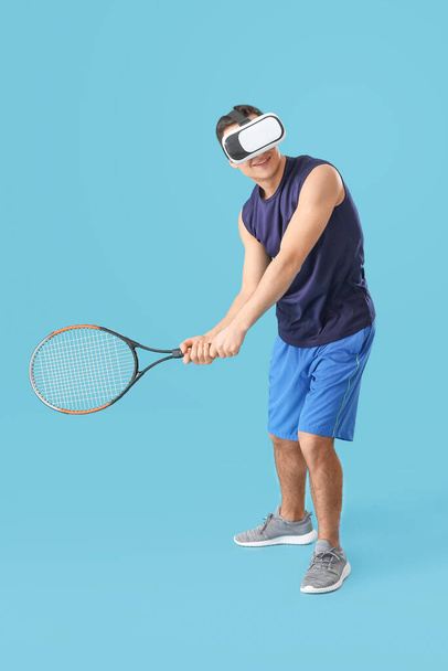 Sporty young man with virtual reality glasses playing tennis on color background - 写真・画像