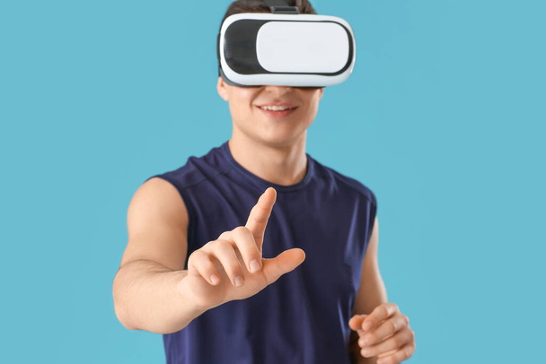 Sporty young man with virtual reality glasses on color background - Photo, Image