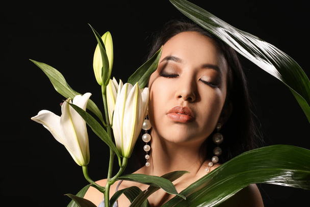 Krásná asijská žena s květinami a tropickými listy na tmavém pozadí - Fotografie, Obrázek