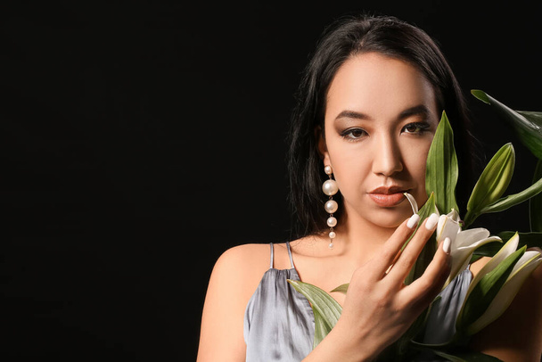 Beautiful Asian woman with flowers and tropical leaves on dark background - Photo, Image