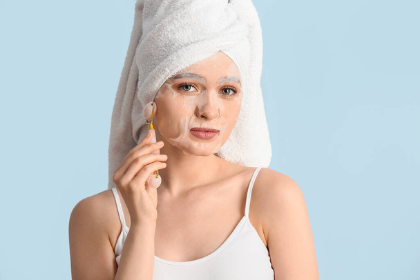 Beautiful young woman with sheet facial mask and massage tool on color background - Photo, Image