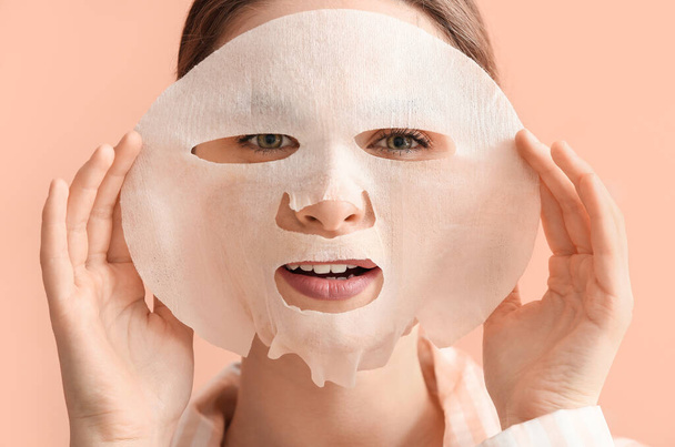 Beautiful young woman with sheet facial mask on color background - Photo, Image