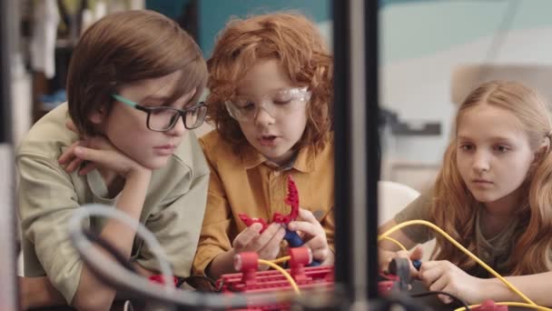Średnie ujęcie trzech białych uczniów ubranych w zwykłe ubrania siedzących razem przy biurku podczas lekcji techniki robotycznej i omawiających swój projekt technologiczny - Materiał filmowy, wideo