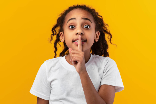 Schwarzes Mädchen legt Finger auf Lippen und macht Schweigezeichen - Foto, Bild