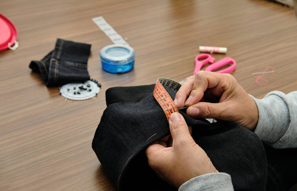 Primer plano de la tela de coser manos femeninas con aguja y cinta métrica en el lugar de trabajo costurera. - Foto, imagen