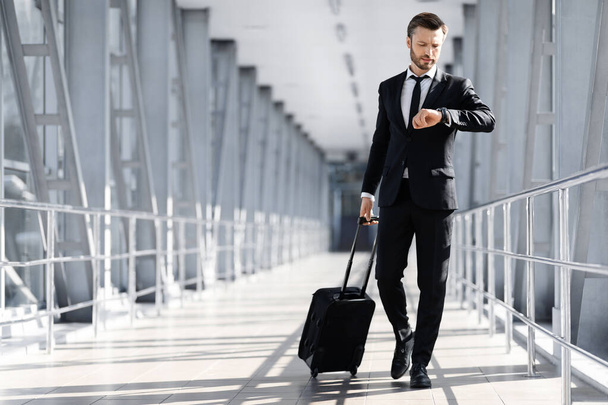 Középkorú üzletember sétál a repülőtér terminál, ellenőrzi az időt - Fotó, kép