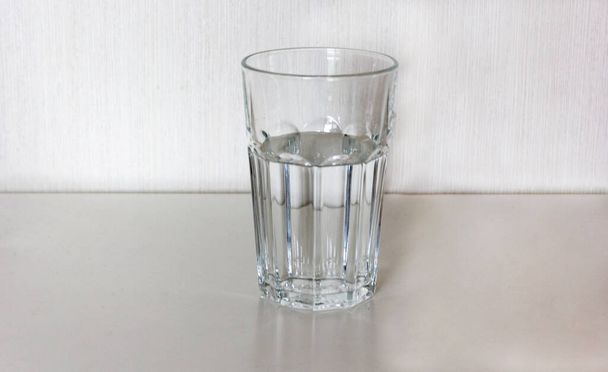 Close-up shot of faceted glass with drinking water on white table with light background - Photo, Image