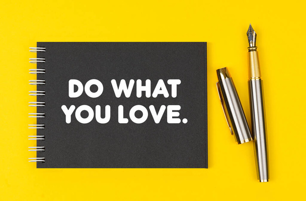 Bedrijfs- en financieel concept. Op een gele achtergrond ligt een pen en een zwart notitieboekje met de inscriptie - Do What You Love - Foto, afbeelding