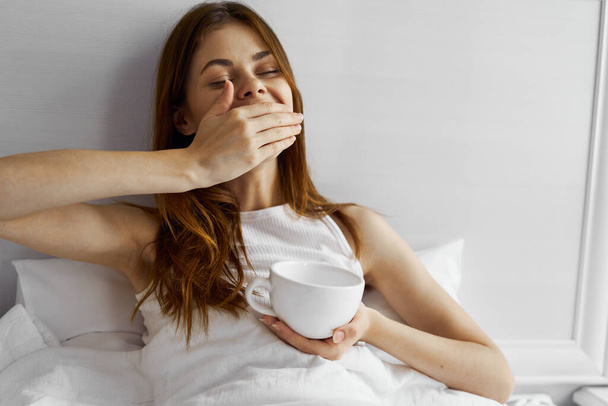 woman lies in bed with a cup in hand morning rest - Photo, Image