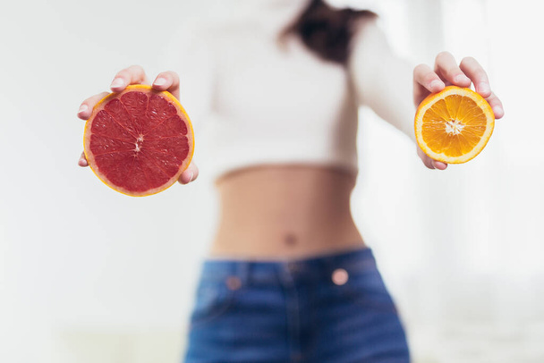 Mujer joven en ropa de fitness sosteniendo toronja y naranja. Concepto de alimentación saludable. - Foto, Imagen