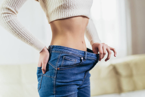 The girl holds jeans in her hand, shows a thin waist Slim female body in large jeans. Diet concept.  - Foto, afbeelding
