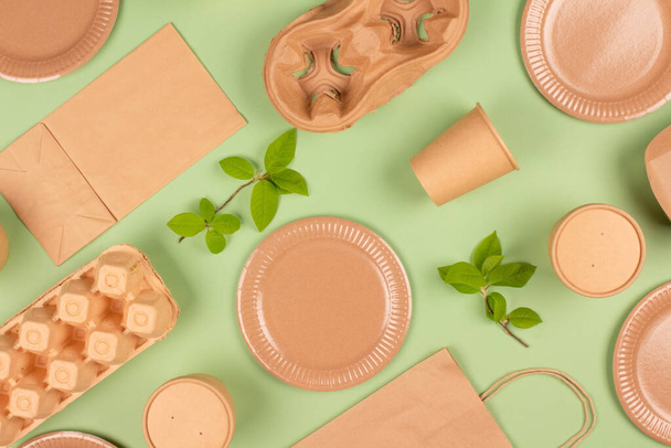Flat lay composition with eco-friendly tableware and kraft paper food packaging on green background. Sustainable packaging, recyclable paperware, zero waste packaging concept. Mockup, selective focus - Photo, image