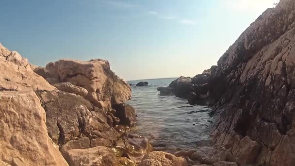 Крупный план скалистого пляжа на море, вода разбивается о берег, хорватский скалистый пляж, безоблачное небо на заднем плане, прекрасный день, прекрасная погода  - Кадры, видео