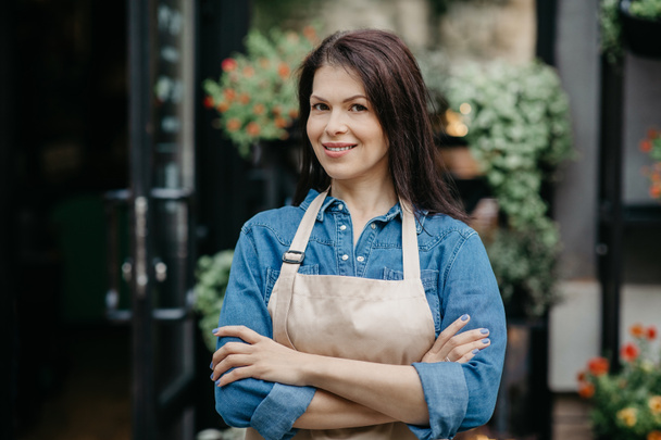 Sorridente giovane attraente donna fiduciosa venditore in grembiule braccia incrociate sul petto - Foto, immagini