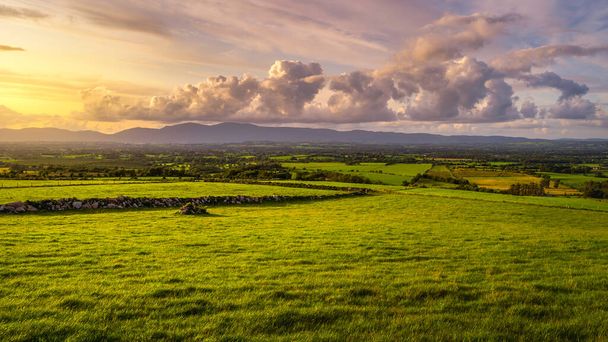 Piękny zachód słońca z dramatycznym niebem o złotej godzinie nad zielonymi polami i farmami w górach MacGillycuddys Reeks, Ring of Kerry, Irlandia - Zdjęcie, obraz