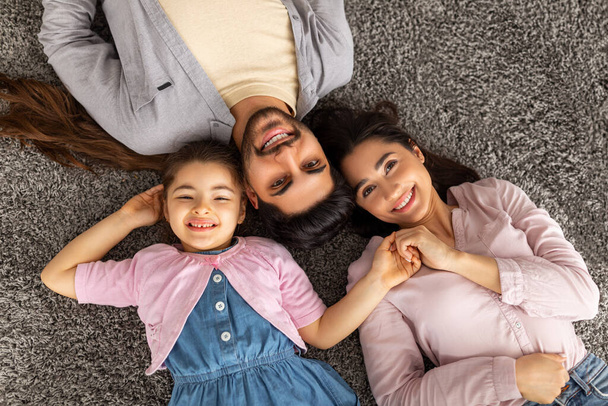 Koncepcja więzi. Nad górnym wysokim kątem widok wschodniej rodziny trzech osób leżących na podłodze dywan razem w domu - Zdjęcie, obraz