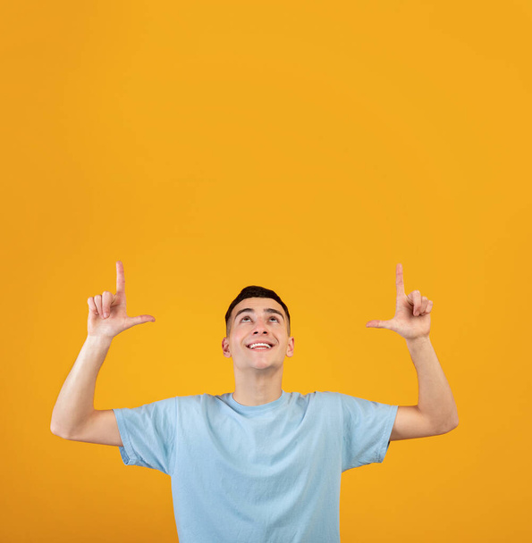 Joyful young guy pointing upwards at blank space for your advertisement on orange studio background. Sale or discount - Foto, Imagem