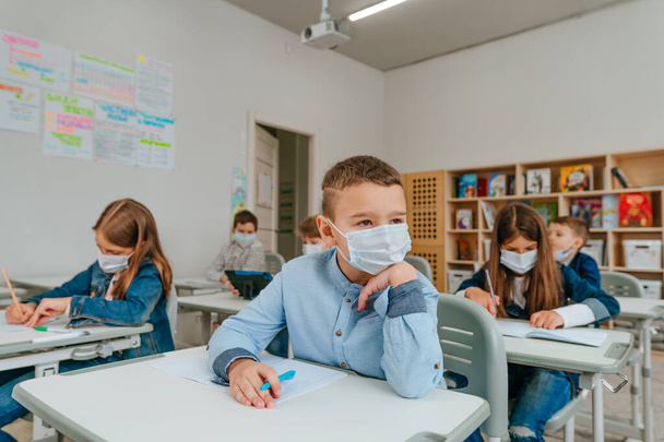 Leerling van de basisschool in de klas tijdens de COVID-19 pandemie. Sociaal afstandelijk concept. Selectieve focus. - Foto, afbeelding