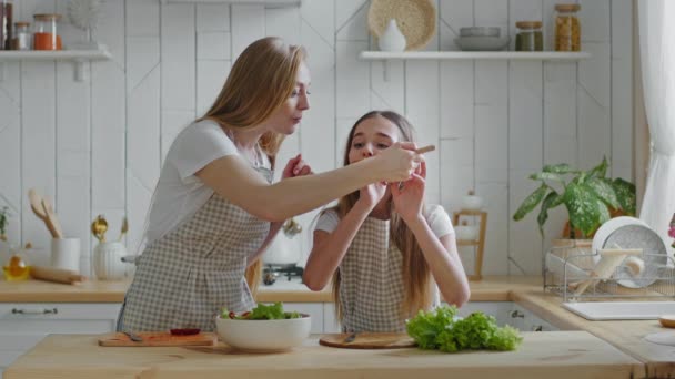 Moeder en dochter koken natuurlijke groente salade, mama voeden baby van houten lepel, meisje eten heerlijke schotel vreugde geeft high five naar vrouw springen met geluk, familie knuffelen in de keuken - Video