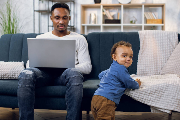 Afro american man working on laptop and taking care of son - 写真・画像