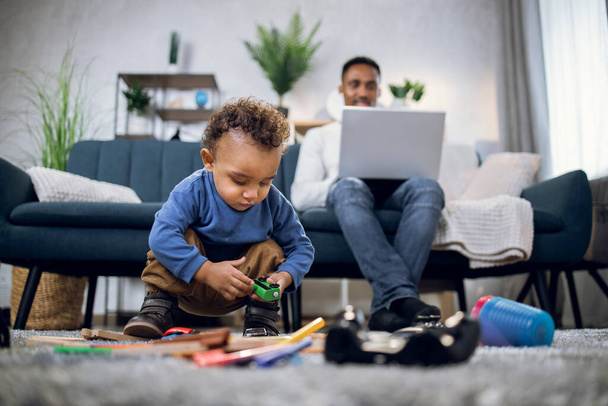 African boy playing with toys while man working on laptop - Valokuva, kuva