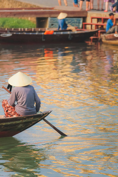 Una mujer vietnamita local con un tradicional sombrero de hoja cónica (non la) paletas en el río Thu Bon en el pintoresco pueblo de la ciudad vieja Hoi An, Vietnam. - Foto, imagen