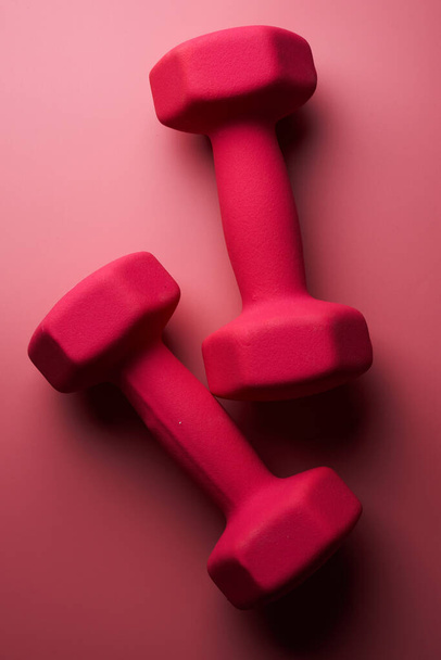 Two pink female dumbbells isolated on pink background close-up with copy space. Fitness concept, weight loss and sport activity - Fotoğraf, Görsel
