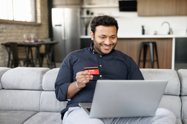 Happy indian guy holding credit card and paying online - Fotoğraf, Görsel