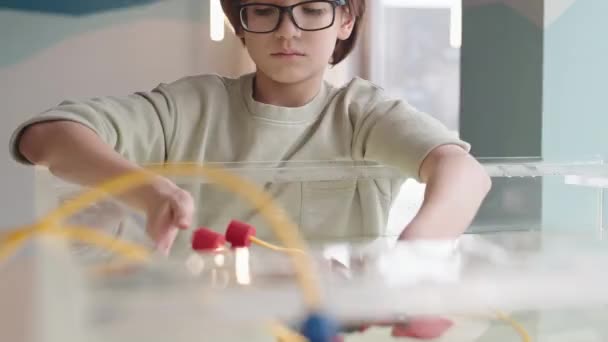 Közepes felvétel kaukázusi tinédzser fiú sötét hajú szemüveges üzembe robo hajó a vízbe, miközben végez kísérletet laboratóriumi iskolában - Felvétel, videó