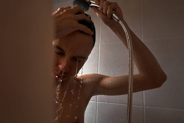 Portrait of young handsome man washes himself with shower gel, lathers head with shampoo in the bathroom at home close-up - Foto, imagen
