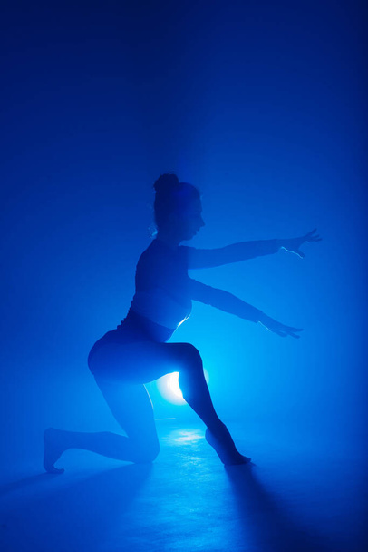 Professionelle Ballerina tanzt Ballett im Rauch. Weibchen im schwarzen Body auf Flutlicht-Hintergrund. - Foto, Bild