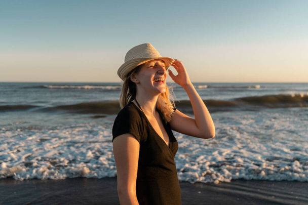 Νεαρή γυναίκα να γελάει και να είναι ευτυχισμένη στην παραλία το ηλιοβασίλεμα. - Φωτογραφία, εικόνα