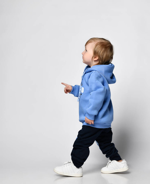 blond little boy in blue t-shirt posing on light background - 写真・画像