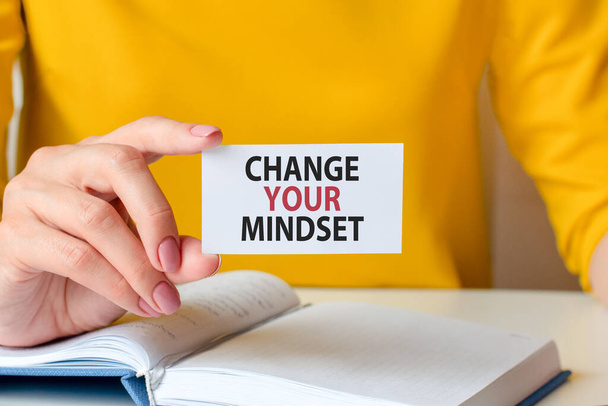 Change your mindset is written on a white business card in a woman's hand. Yellow background. Business and advertising concept - Photo, Image