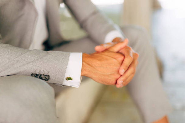 A man in a gray suit in a white shirt with cufflinks sits with folded hands, close-up - Φωτογραφία, εικόνα