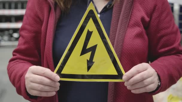 A nő sárga háromszögletű jelet tart, amire villámot festettek. Nagy voltos - Felvétel, videó