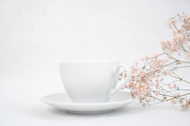 a cup of black coffee on a white table and with a sprig of dried flowers - Foto, Imagen