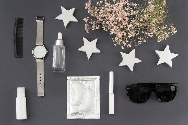 trendy flat lay: eye patches, cream, lipstick, wristwatch, sunglasses and a bouquet of dried flowers - Photo, Image