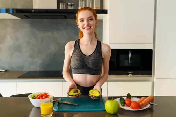 Sportliche Frau mit Turnkleidung isst Früchte in der Küche - Foto, Bild