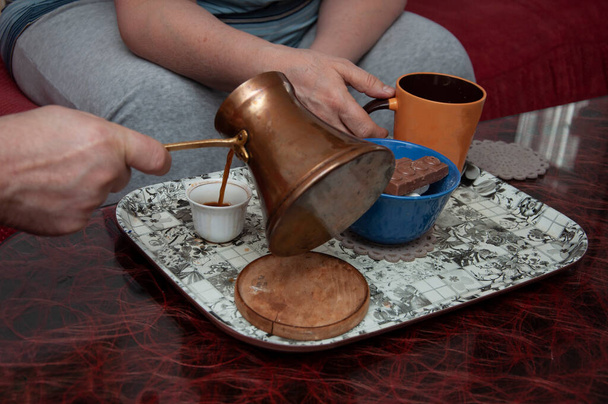 The male hand is pouring bosnian, turkish coffee in cup of coffee and woman hand holding espresso cup - Photo, Image