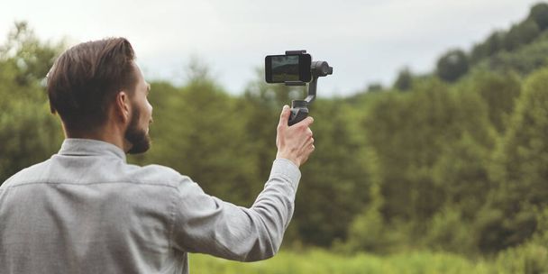 Zadní pohled na tisíciletého muže nahrávajícího video na smartphonu se stativem - Fotografie, Obrázek