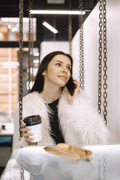 Girl in a cafe drinks coffee with phone - Fotoğraf, Görsel