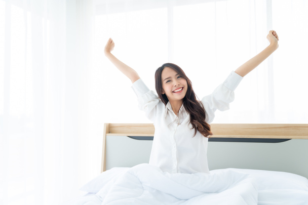 Schöne asiatische Frauen wachen morgens im Schlafzimmer auf. Sie trägt weißes Kleid, das den Körper dehnt und sich frisch anfühlt - Foto, Bild