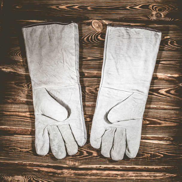 Λευκά δερμάτινα γάντια συγκόλλησης σε ξύλινο φόντο. Φωτογραφία στούντιο με σκληρό φωτισμό. - Φωτογραφία, εικόνα