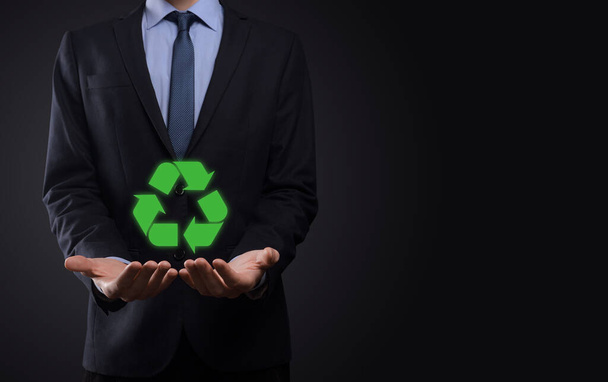 Businessman in suit over dark background holds an recycling icon, sign in his hands. Ecology, environment and conservation concept. Neon red blue light. - Zdjęcie, obraz